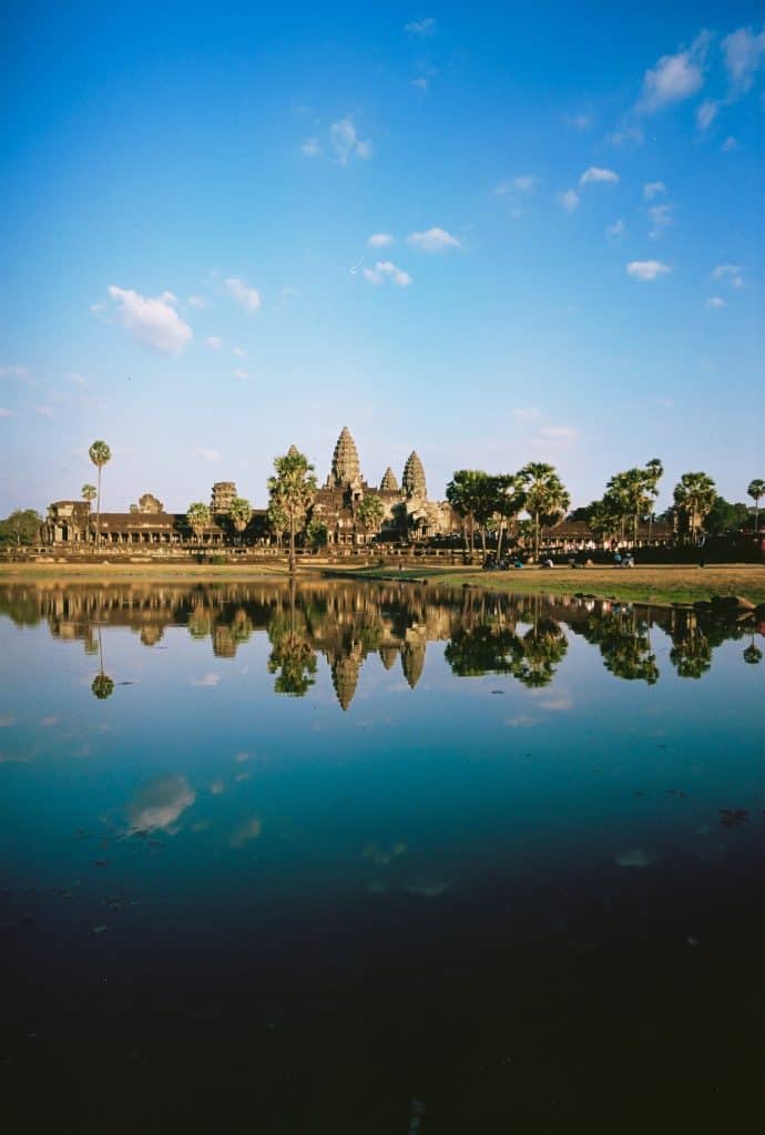 Angkor Wat in Cambodia in the background with a blue body of water in the foreground and open blue skies