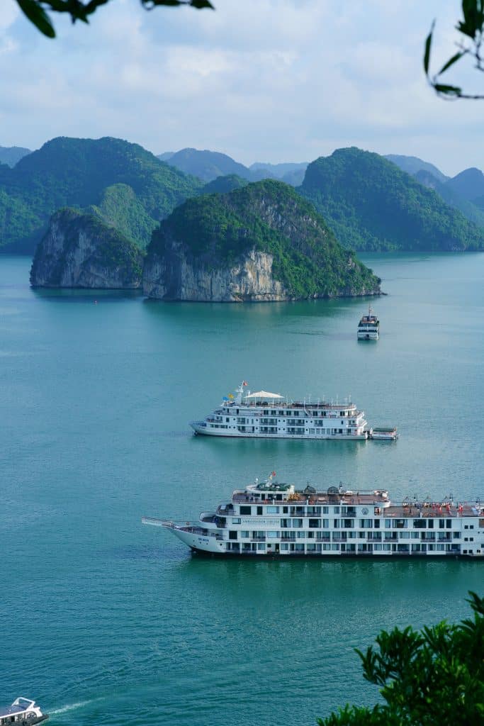 two cruise ships passing by in Halong Bay, Vietnam with green mountains in the back.