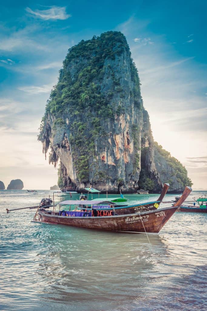 giant boulder in the water of Thailand with a boat in the foreground tied off.